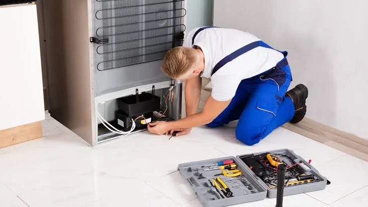 Technician testing components at the back of a refrigerator